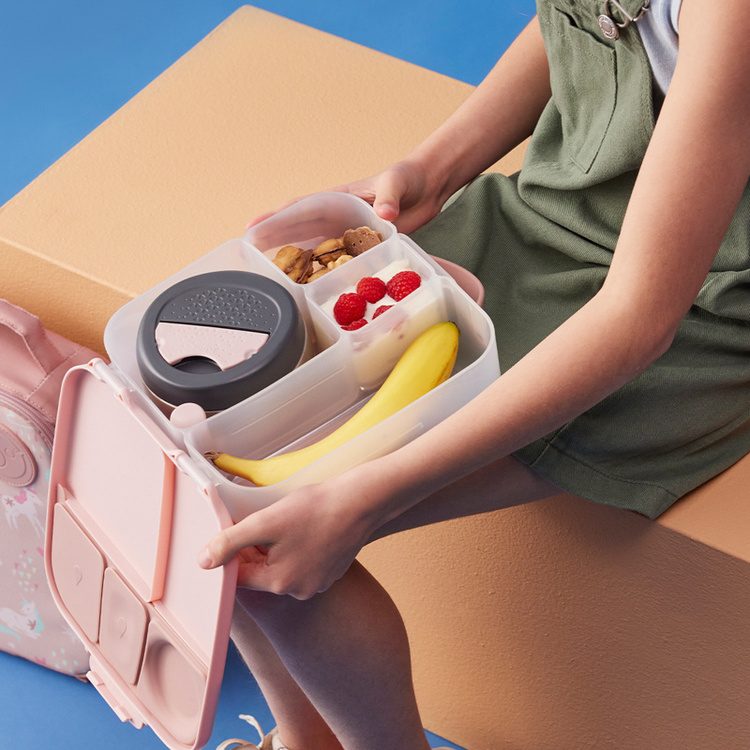 Różowy lunchbox b.box w rękach dziecka — przegródki z owocami