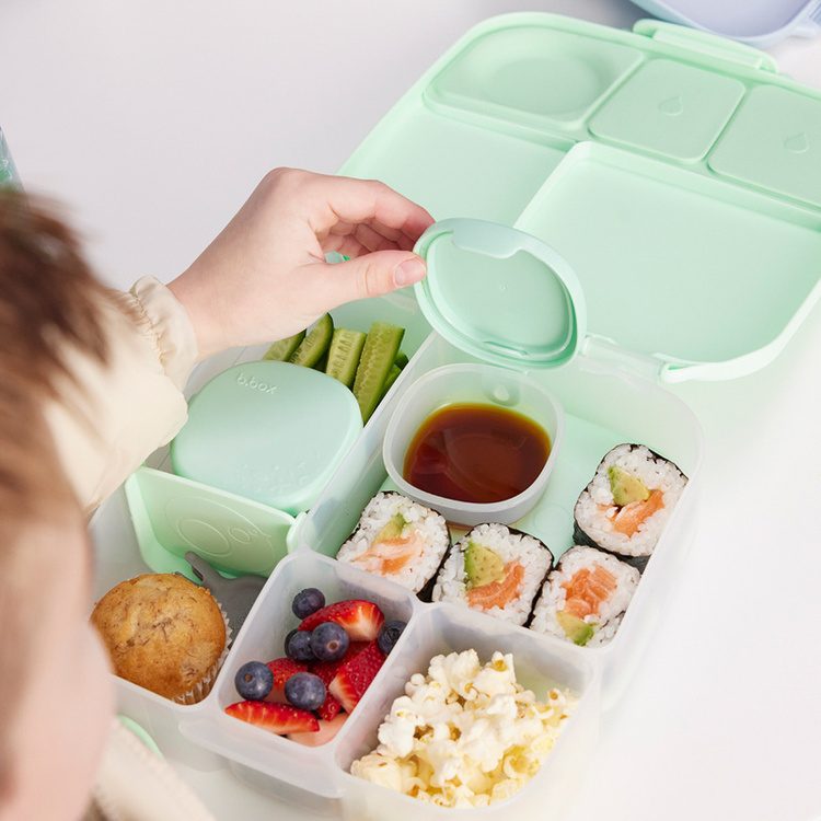 Miętowy lunchbox b.box — dziecko otwiera pojemnik z przekąskami